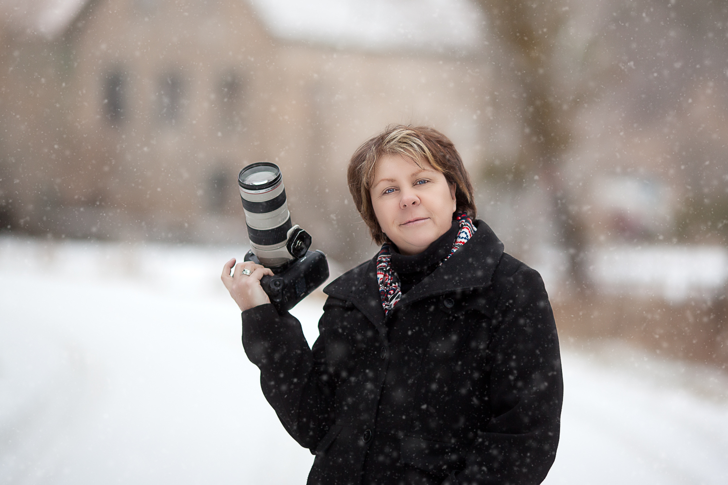 Sandra Randall, Photographer standing holding a camera in the snow with a black jacket on.